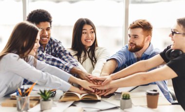 Mutlu grup arkadaşları birliklerini göstermek için el ele tutuşuyorlar. Üniversite kütüphanesinde final sınavlarına hazırlanıyorlar.