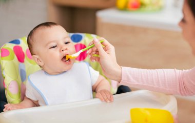 Bir anne ve oğlu, bebek yüksek sandalyede otururken mutfakta yemek yiyorlar. Atmosfer besleyici ve samimi, aile sıcaklığını yansıtıyor..