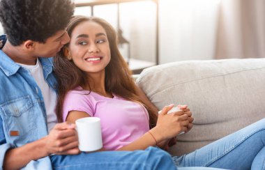 Afro-Amerikalı genç çift oturma odasında bir kanepede oturuyor. Adam elinde bir kupa kahve tutuyordu ve kıza bakıyordu. İkisi de rahat ve memnun görünüyorlar. Oda aydınlık ve havadar..