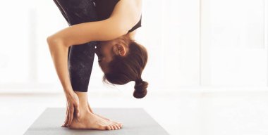 Bir kadın içeride yoga yaparken görülüyor, öne doğru kıvrılmış pozlar veriyor. Ayar, büyük pencerelerden gelen doğal ışık ve kopyalama alanı olan bir panorama ile aydınlık.