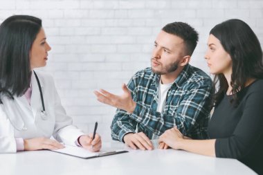 Genç bir çift beyaz tuğlalı bir ofiste bayan bir doktorun karşısında oturuyor. Hasta adam konuşuyor, eliyle işaret ediyor, ortağı ise dikkatle dinliyor. Doktor not defterine not alır.