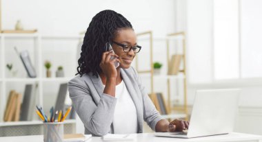 Çekici Afrikalı Amerikalı iş kadını rahat ofiste birden fazla iş yapıyor, dizüstü bilgisayar kullanıyor ve telefonla konuşuyor, boşluğu kopyalıyor