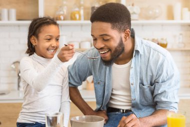 Neşeli bir Afrikalı Amerikalı kız, babasına mutfakta kahvaltı hazırlıyor. Aileyi ve babalığı simgeliyor.