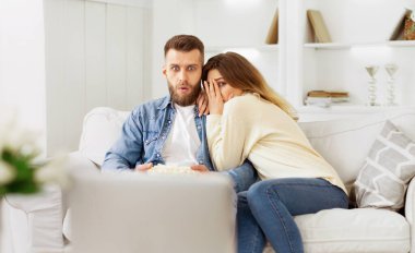 Bir adam ve bir kadın oturma odasındaki bir kanepede oturuyorlar..