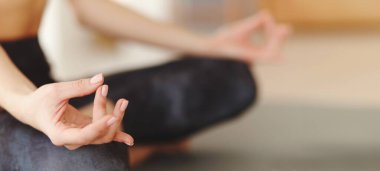 Bir kadın yoga minderinde bağdaş kurup meditasyon çalışmalarına odaklanır. Ellerini Mudra pozisyonunda tutuyor, huzurlu ve huzurlu bir atmosfer yaratıyor..