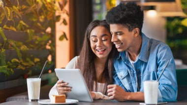 Genç siyahi bir adam ve kız kafeterya masasında oturuyorlar, tablet bilgisayarın içinde. Ekrana bakarken bir şeyi tartışıyor gibi görünüyorlar, ara sıra tıkırdıyor ve çalıyorlar..