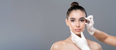 Saçları topuz şeklinde olan genç bir kadın klinikte bir dermatolog tarafından muayene ediliyor. Beyaz eldiven giyen dermatolog herhangi bir anormallik var mı diye cildini yakından inceliyor.