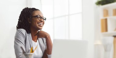 Moda ofis ortamında dizüstü bilgisayarı üzerinde çalışan Afrikalı Amerikalı iş kadını, fotokopi odasına bakıyor.