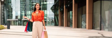 Alışveriş ve Satış Sezonu. Modern alışveriş merkezleriyle dolu renkli alışveriş torbalarıyla alışveriş yapan mutlu bayan alıcı, uzaklara bakıyor, reklam teklifleri sunuyor. Tüketim ve Alışveriş, Boşluğu Kopyala