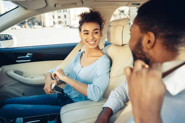 stock image The image shows African American woman fastening her seatbelt in the passenger seat of a car. She is looking at the man sitting in the drivers seat, who is looking at her and smiling