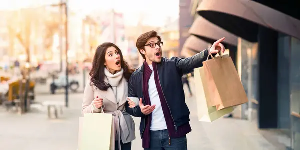 stock image A couple holding multiple shopping bags in their hands, pointing excitedly at something off-camera.