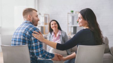 Bir çift terapi seansında yüz yüze oturur, el ele tutuşurlar. Kadın ortağına gülümserken, adam mutlu ve rahat görünüyor. Arkalarında bir bayan danışman oturuyor.