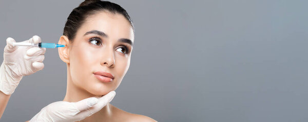 A young woman undergoes a cosmetic injection on her face, administered by a professional wearing gloves. She looks calm and composed as the procedure takes place in a clinical setting.