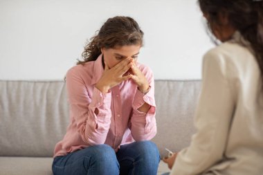 Bir kadın kanepede oturur ve ellerini yüzüne doğru tutar. Bir terapist yanında oturur ve onu dinler. Sıkıntılı ya da bunalmış gibi görünüyor..