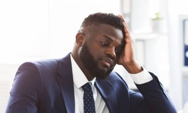 Yorgun, genç, Afro-Amerikan iş adamı. Dizüstü bilgisayarla çalışıyor. Alnına dokunuyor, uzayı kopyalıyor.