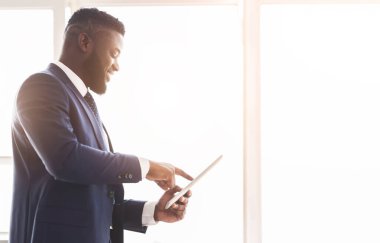 Neşeli Afrikalı Amerikalı girişimci dijital tablet üzerinde iş uygulaması kullanıyor, ortaklarla konuşuyor, boş alan