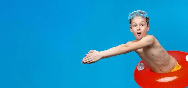 stock image Funny diver. Emotional boy in inflatable ring and swim goggles diving aside, blue panorama background with free space