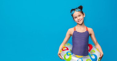 Mavi ve beyaz çizgili mayo giyen genç bir kız büyük şişme bir şamandıra tutarken görülüyor. Havuzda ya da plajda güzel bir gün geçiriyor gibi görünüyor.