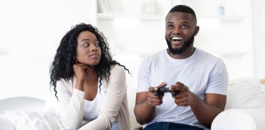 Bir çift kanepede oturuyor, erkek video oyunu oynamaya dalmış, kadın ise can sıkıcı bir bakışla izliyor..