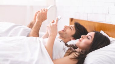 Bir çift yatakta yatıyor, ikisi de sabahları akıllı telefonlarını kullanıyor. Kadın kameraya dönük bir şekilde yan yatarken, adam kameraya dönük bir şekilde sırt üstü uzanıyor..