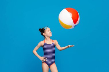 Mayolu genç bir kız kumlu sahilde renkli bir plaj topuyla enerjik bir şekilde oynuyor..