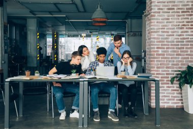 Üniversite kütüphanesi. Öğrenciler grup çalışması yapıyor, dizüstü bilgisayar kullanıyorlar, boş alan var.