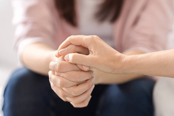 Два человека сидят близко, предлагая утешение через рукопожатие. Их переплетающиеся руки означают поддержку и сочувствие, создавая уютную атмосферу в помещении, обрезанные