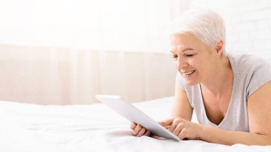 Gülümseyen ve onun torunları dijital tablet, boş alanı olan panorama resimleri izlerken, yatakta mutlu kadın kıdemli