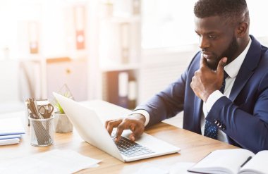Yoğunlaşmış genç siyah yönetici internette araştırma yapıyor, dizüstü bilgisayar kullanarak, alanı kopyalayarak