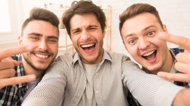 Üç neşeli arkadaş birlikte poz veriyor, neşeli bir anı paylaşıyorlar parlak ifadeler ve jestlerle