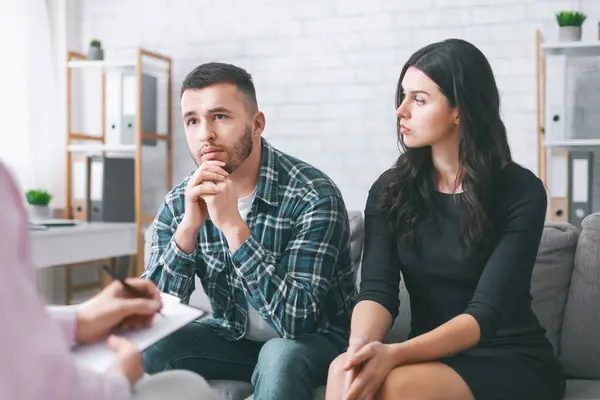 stock image A young couple sits on a couch in an office setting, listening attentively to an off-camera therapist. They appear to be in a serious discussion