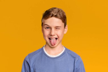 Oyuncu genç çocuk göz kırpma ve dil, turuncu stüdyo arka plan dışarı yapışma