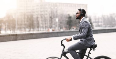 Bir Afrikalı Amerikalı işadamı modern bir şehir üzerinden ofise bisikletle gidiyor. Sahne dinamik ve hareketli, profesyonel hayatla çevre dostu seyahat arasındaki dengeyi gösteriyor..