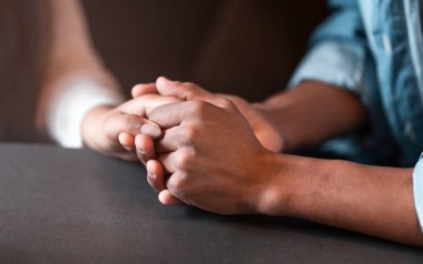 İki kişi bir masada oturuyor, el ele tutuşuyorlar. Birbirlerine kenetlenmiş parmakları bir bağlantı ve yakınlık hissi veriyor. Masa basittir, insan etkileşimine odaklanır..