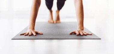 Kırpılmış bir kadın gri bir mindere yoga pozu verirken dengesini koruyor ve odaklanıyor. Çıplak ayakları ve elleri yüzeye bastırılmış. Bu da kuvvetini ve esnekliğini gösteriyor.