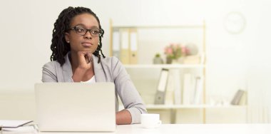 Hayalperest siyah kadın bir ofis ortamında dizüstü bilgisayar kullanıyor. Çevre profesyonel ve düzenli, modern dekor ve düzenli bir masa ile, iş odaklı, kopyalama alanı