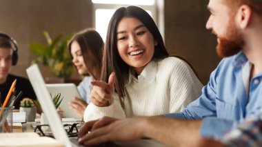 Üniversite öğrencileri kütüphanede dizüstü bilgisayar kullanıyor, okul ödevi için çalışıyor, birlikte tartışıyorlar.