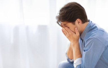 Bir adam pencerenin önünde oturuyor, başı eğik ve elleri yüzünü örtüyor, üzüntü ve umutsuzluğu ifade ediyor..