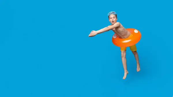 stock image Teen boy in inflatable ring about to dive into swimming pool, blue studio background