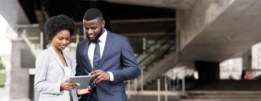 Dijital tablet kullanan ve yeni proje detaylarını açık havada tartışan koyu tenli iş adamları