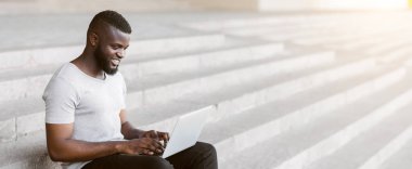 Genç bir adam beton merdivenlerde oturur ve dizüstü bilgisayarıyla çalışır..