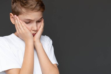 Yüzü ellerinde üzgün bir genç, gri bir arka planda soyutlanmış, genç bir duygusal anı canlandırıyor.