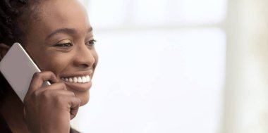 Profesyonel elbiseli parlak Afro-Amerikan kadın, ofis penceresinden yönetiyor, telefonla konuşuyor, yakın plan, kopyalama alanı.