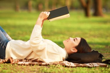 Asyalı bir kadın yerde uzanıyor, okuduğu bir kitaba dalmış. Etrafı sakin bir ortamla çevrili ve kendini hikayeye kaptırıyor..