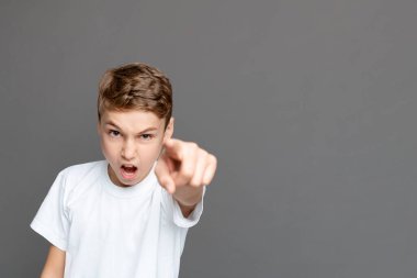 İddialı bir ifadeye sahip genç bir çocuk doğrudan kamerayı işaret ediyor. Doğruluk ya da ithamda bulunuyor. Gri bir arkaplana karşı izole bir şekilde duruyor.