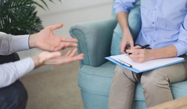 Gündüz güneşli bir öğleden sonra modern bir ofiste bir adamla terapi seansında not alırken aktif olarak dinleyen terapist.