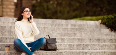 Dışarıdaki beton merdivenlerde oturan Asyalı kadın cep telefonuyla sohbet ediyordu. Telefonu kulağına dayamış, yüzünde odaklanmış bir ifadeyle..