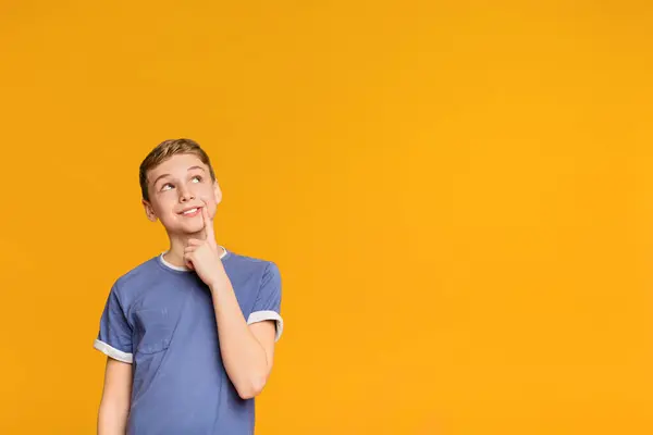 stock image Tricky boy thinking about some prank, looking up at free space on orange background