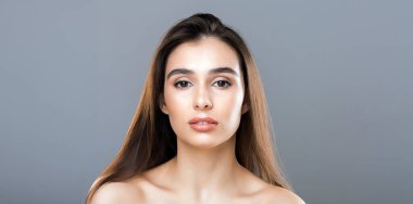 Uzun, kahverengi saçlı ve tarafsız bir yüzü olan genç bir kadın doğrudan kameraya bakar. Basit, gri bir arkaplanda poz veriyor ve sakin, zarif bir tavır sergiliyor..