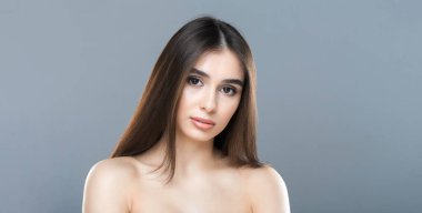 Akan, uzun saçlı bir kadın fotoğraf için poz veriyor. Kendinden emin ve dengeli görünüyor, bir eli kalçasında ve yüzünde hafif bir gülümsemeyle. Arka plan basit.